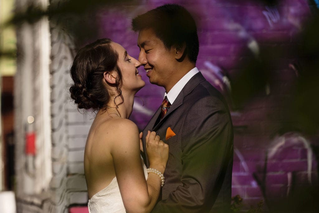 bride and groom stand nose to nose laughing in front of Ottawa Chinatown gaffiti
