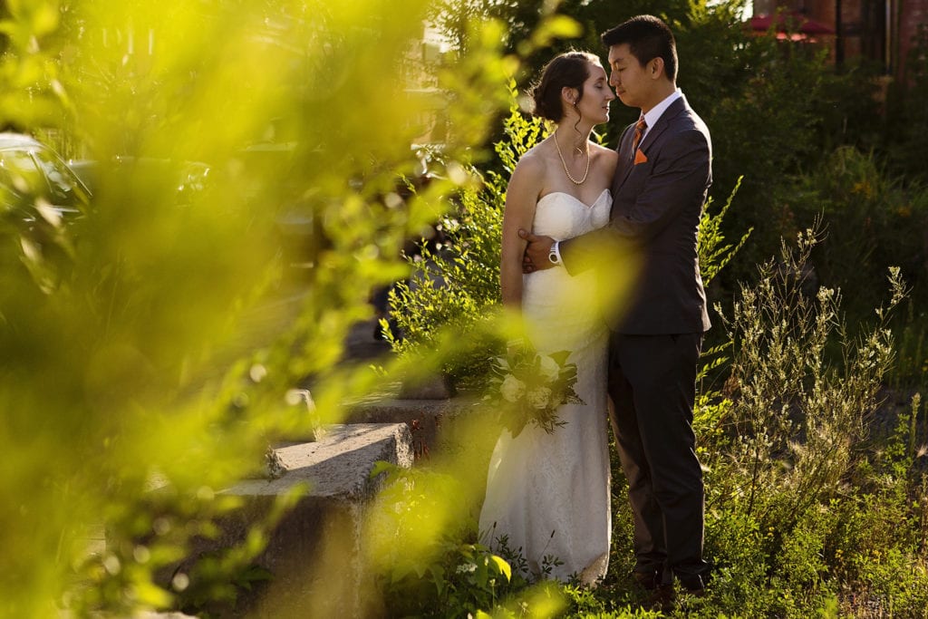 bride and groom stand close together in overgrown parking lot