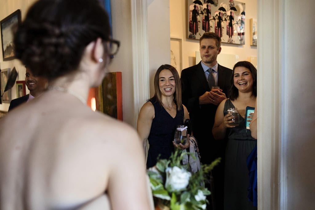 three wedding guests look at bride as she enters Orange Art Gallery wedding reception