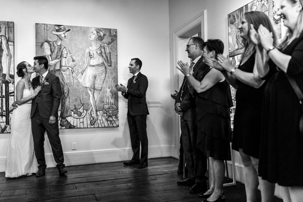bride and groom kiss as onlookers applaud during Orange Art Gallery wedding reception
