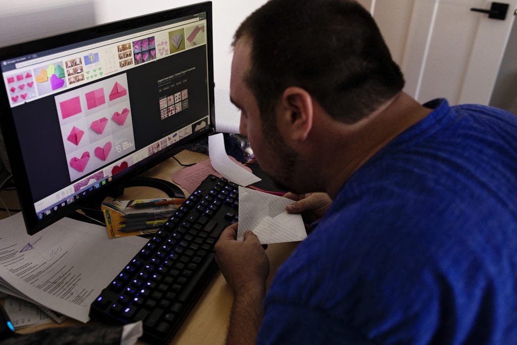 groom looks at origami instructions on computer while trying to fold letter