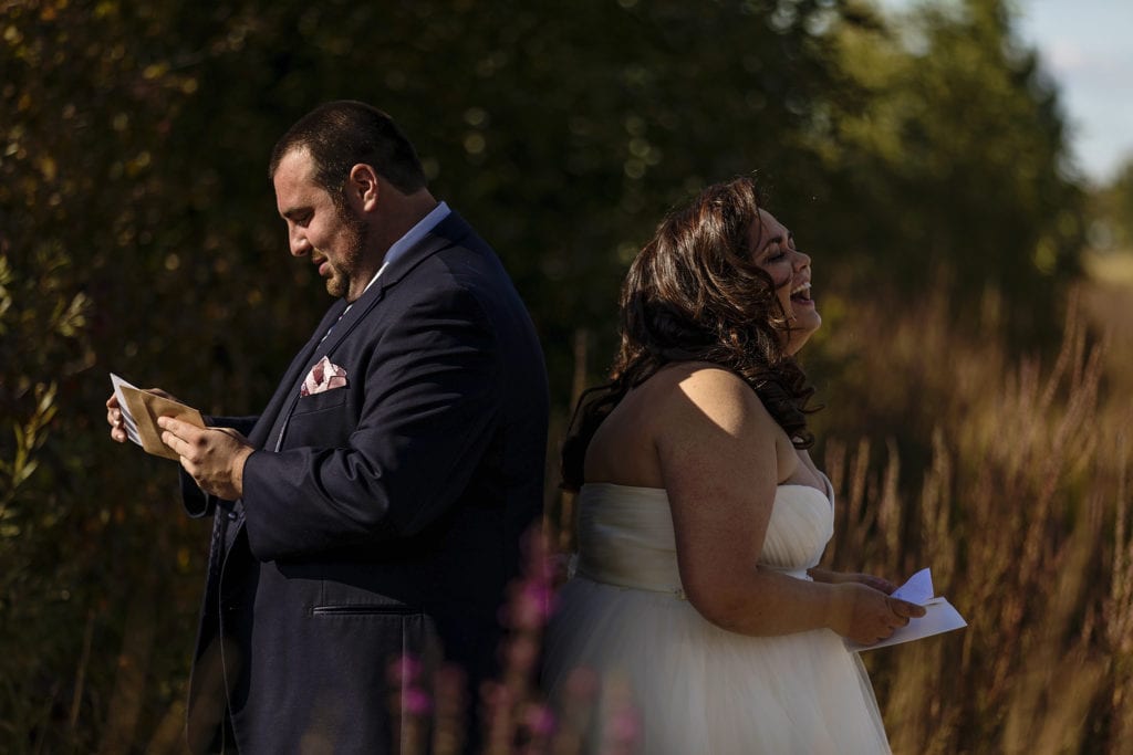 bride and groom stand back to back with letters while bride laughs
