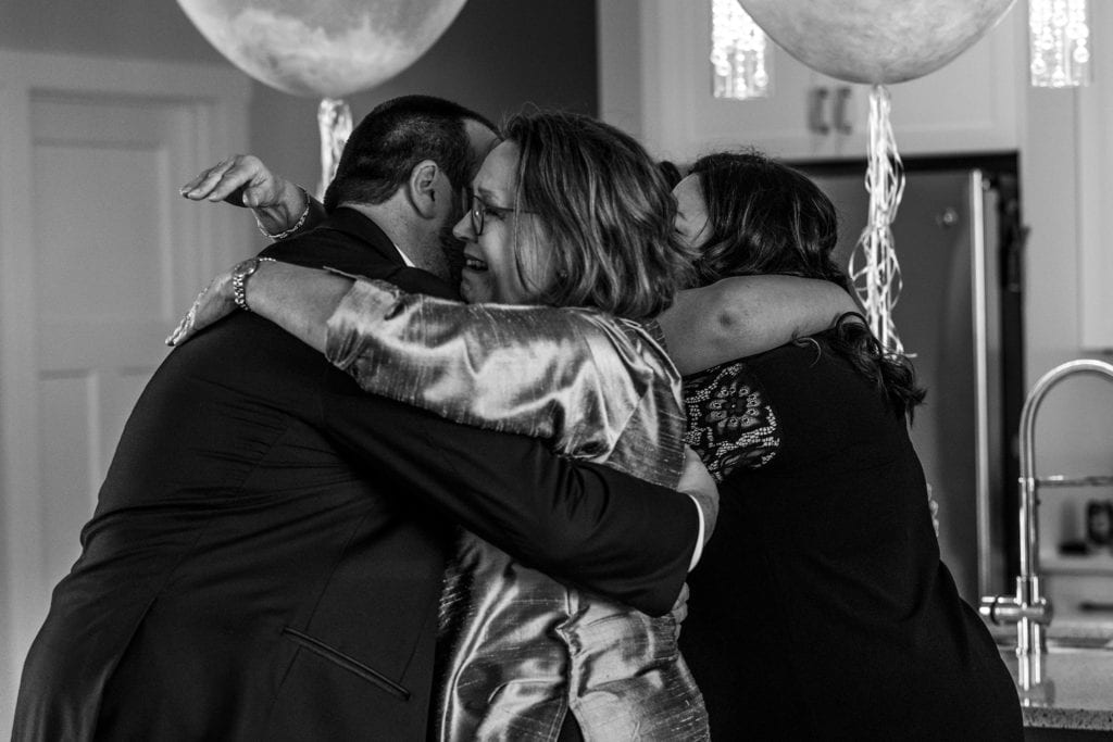 woman cries as she hugs groom and bride receives hug in background