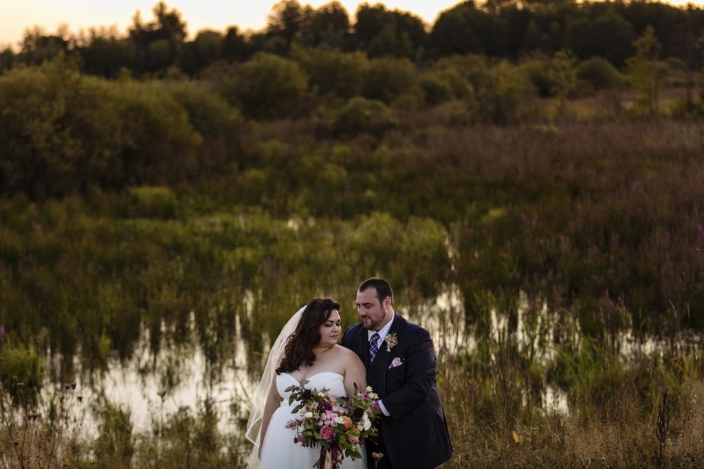 bride and groom stand close together in front of marshy field