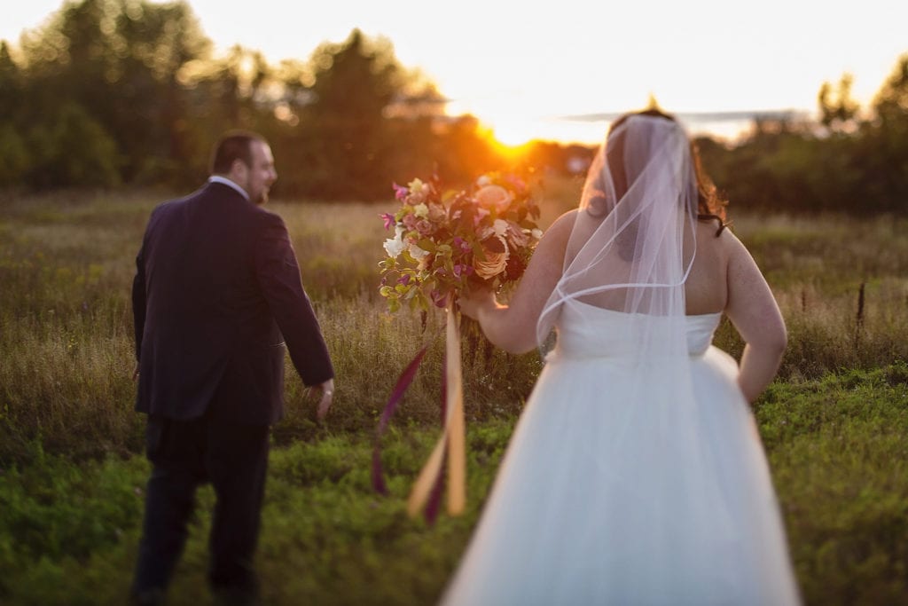 bride and groom walk towards field and setting sun