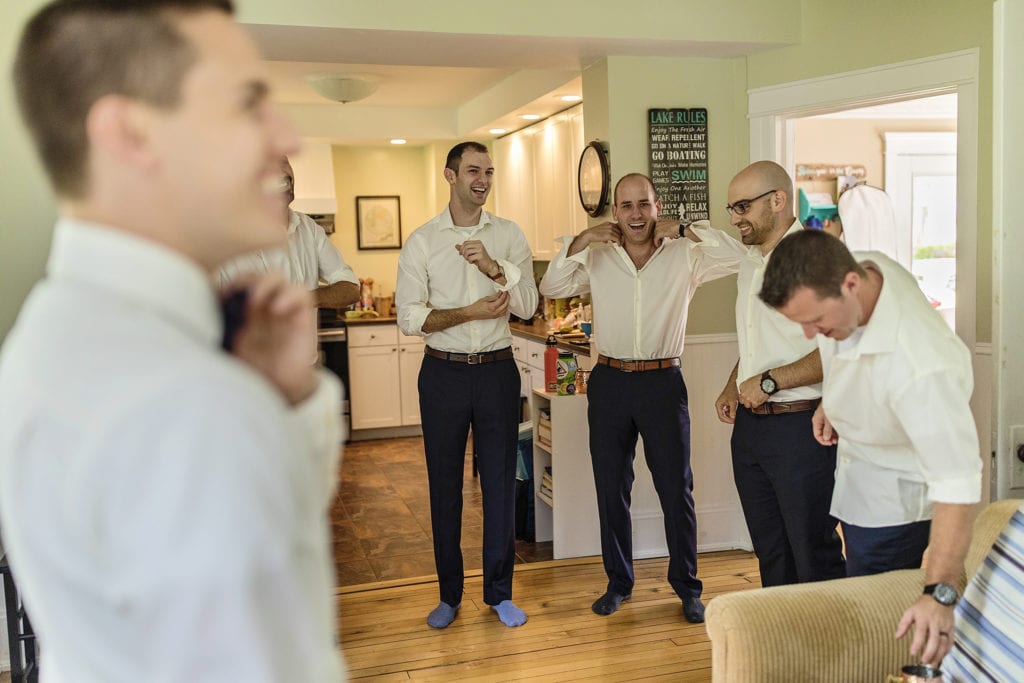 groomsmen laugh as they button shirts during wedding prep