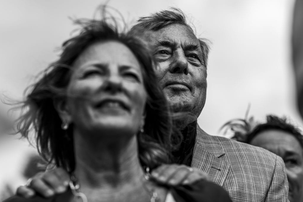 father of the groom watches Point Petre wedding ceremony while resting hands on wife's shoulders