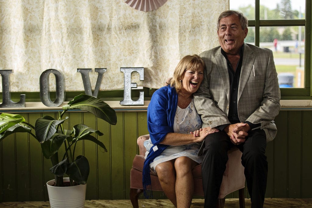couple sit on armchair next to love sign and laugh heartily