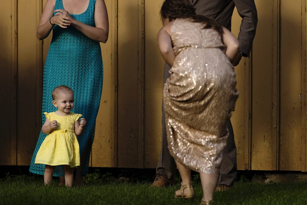 bridesmaid crouches and approaches smiling toddler in yellow dress