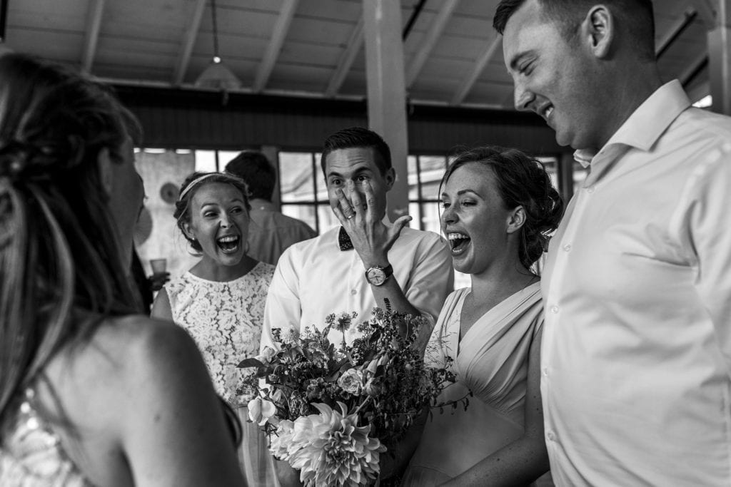 groom holds up hand to show ring while others laugh