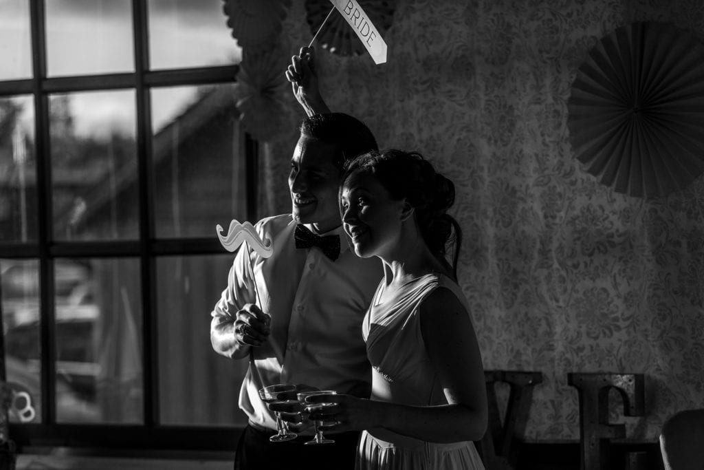 bride and groom stand using photo booth props including sign that says bride