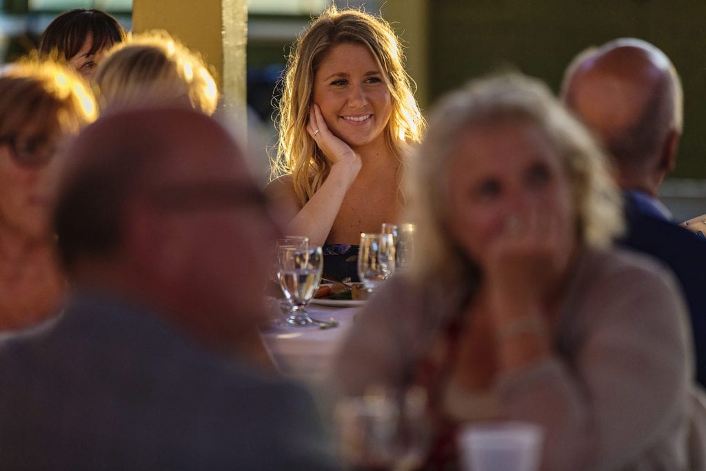 woman rests hand on cheek while smiling during wedding speeches