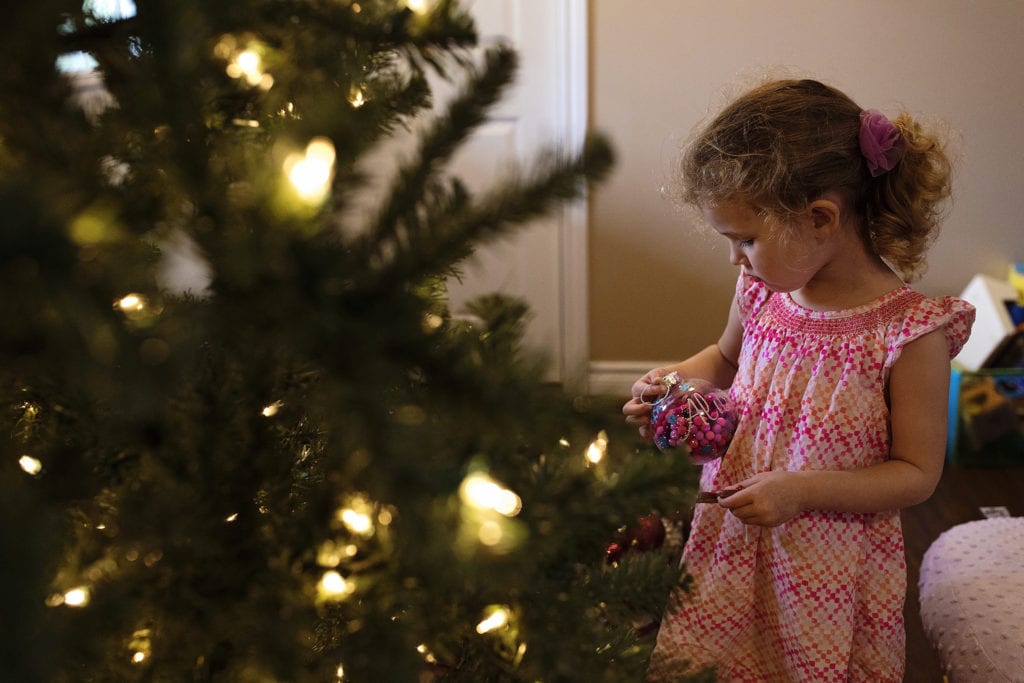 Girls stands in front of tree holding ornament as part of Cornwall family Christmas preparations