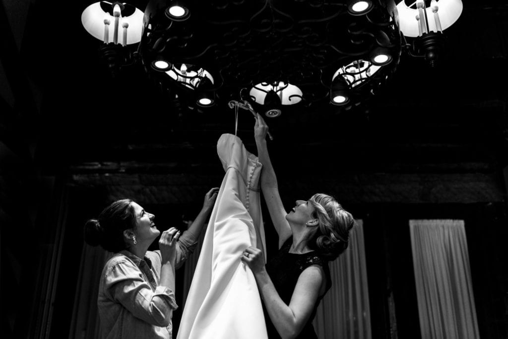 bride and friend hang dress from chandelier
