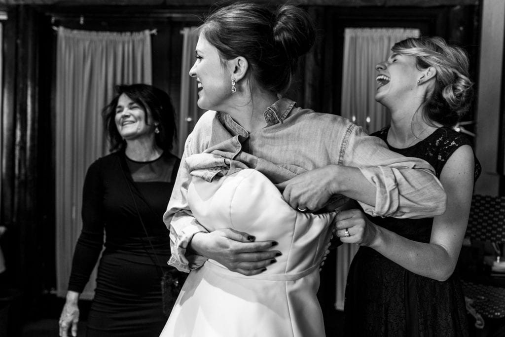 women laugh as bride is helped into her dress