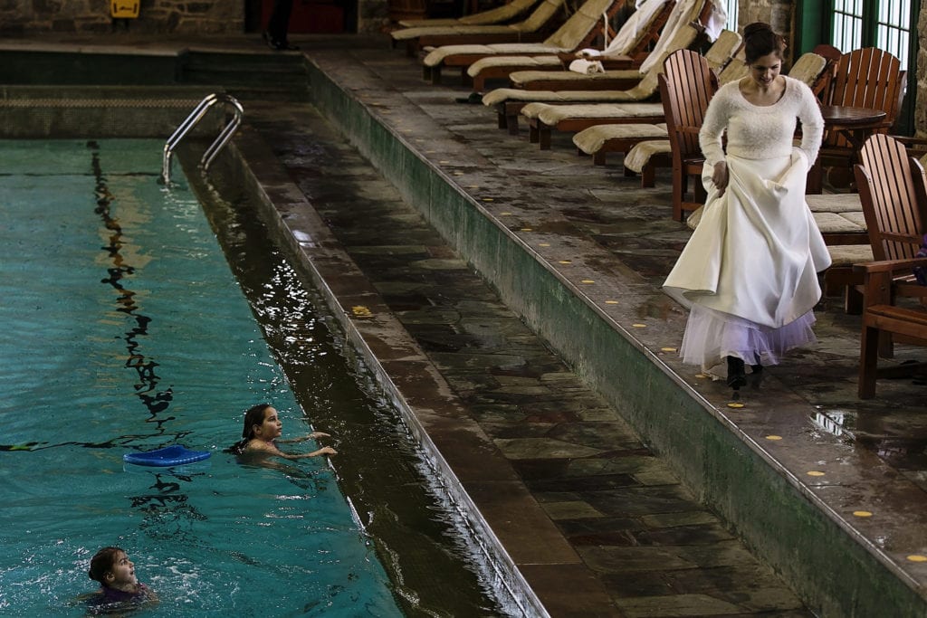 bride walks past girls swimming in pool