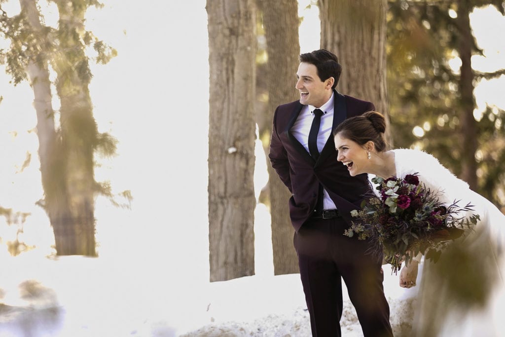 bride doubles over with laughter while groom adjusts trousers