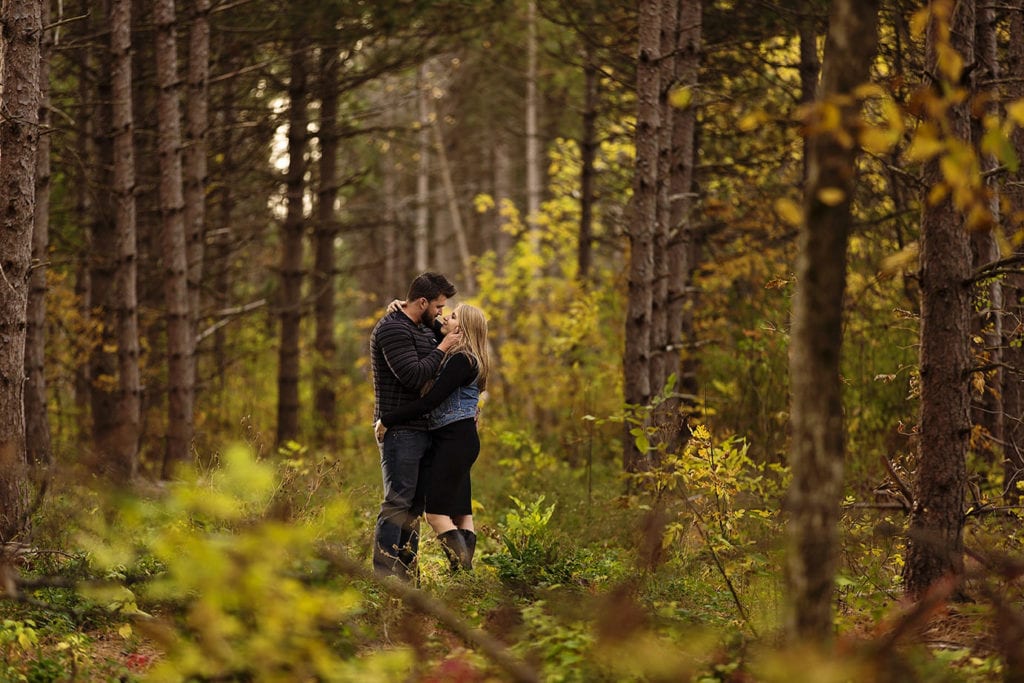 young couple embracing in fall colored forest during woodsy engagement shoot