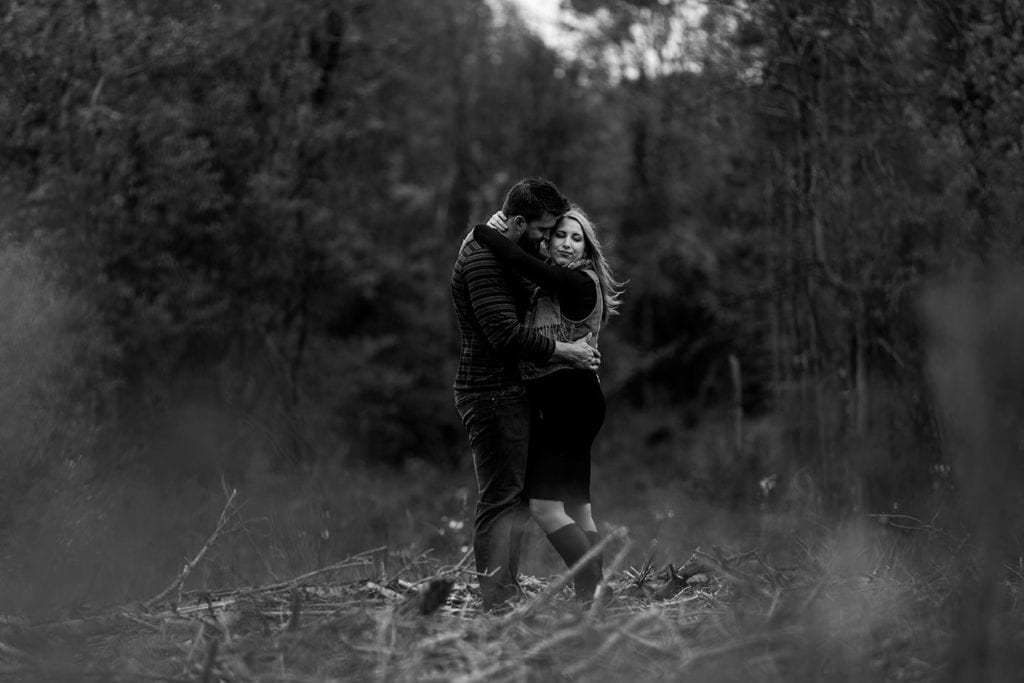 couple embracing in forested area during woodsy engagement shoot