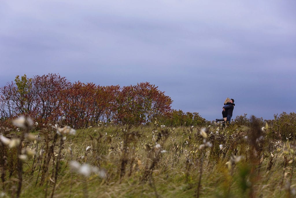 couple in fall field under dark skies in woodsy engagement session