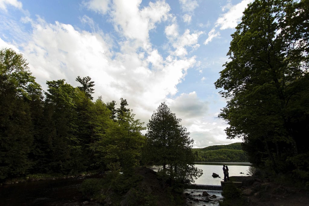 couple embracing on shore of forested lake in Gatineau Park engagement session