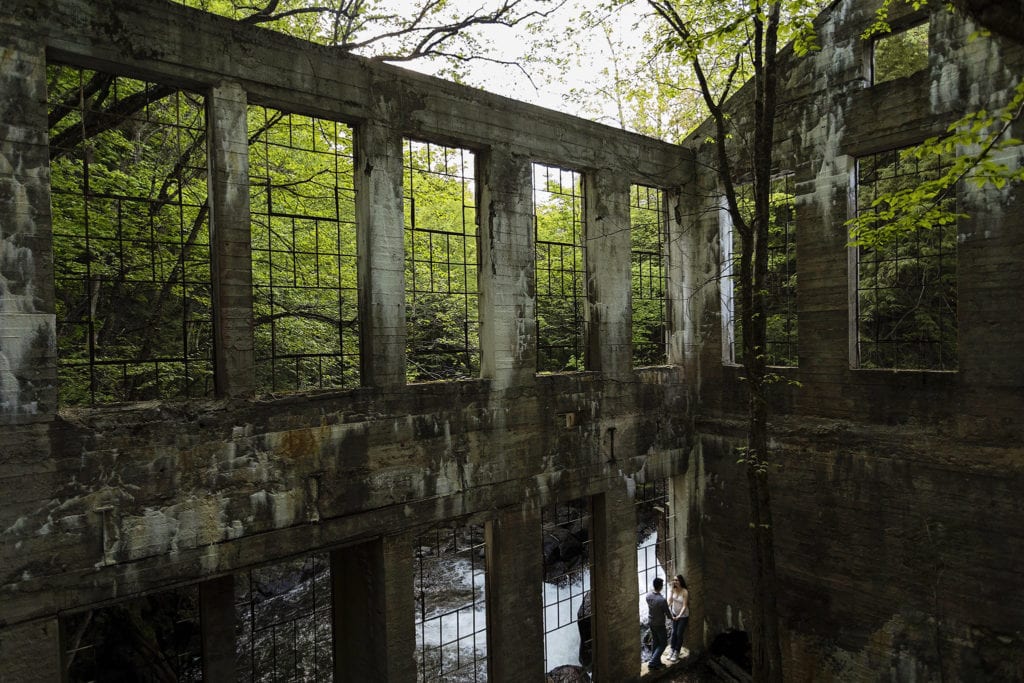 couple leaning in window well of ruins beside waterfall in Gatineau Park engagement session