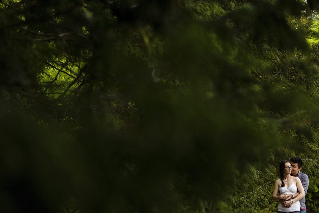 couple with matching watches embracing in forest at Gatineau Park engagement session