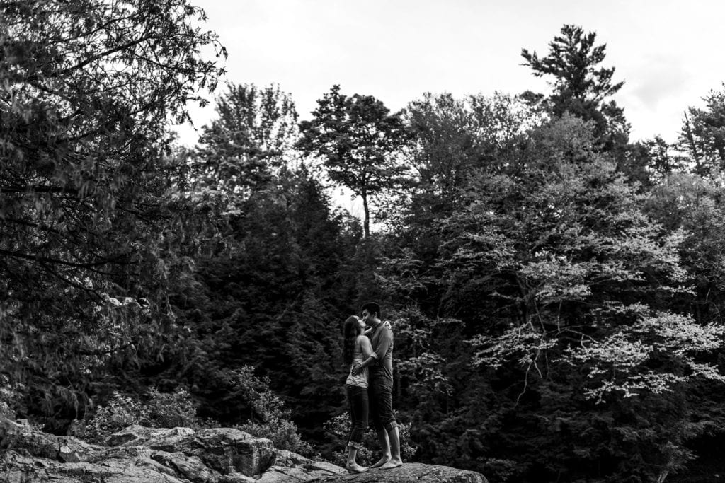 young couple kissing atop rock in Gatineau Park engagement session