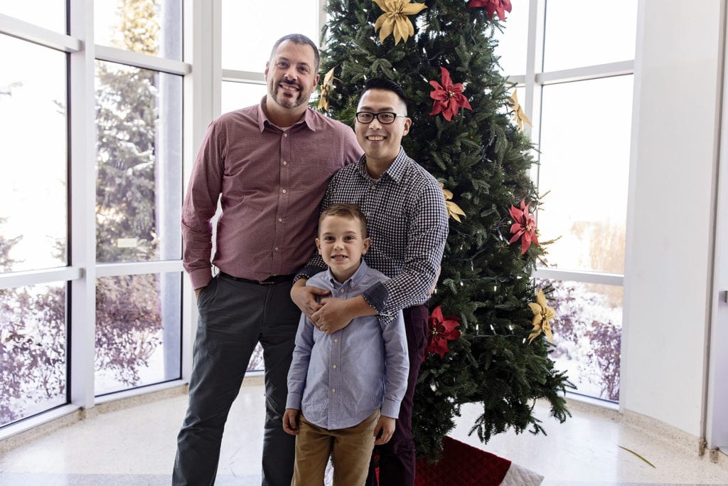 same-sex couple and adoptive son smiling in front of Christmas tree on Adoption day in Cornwall