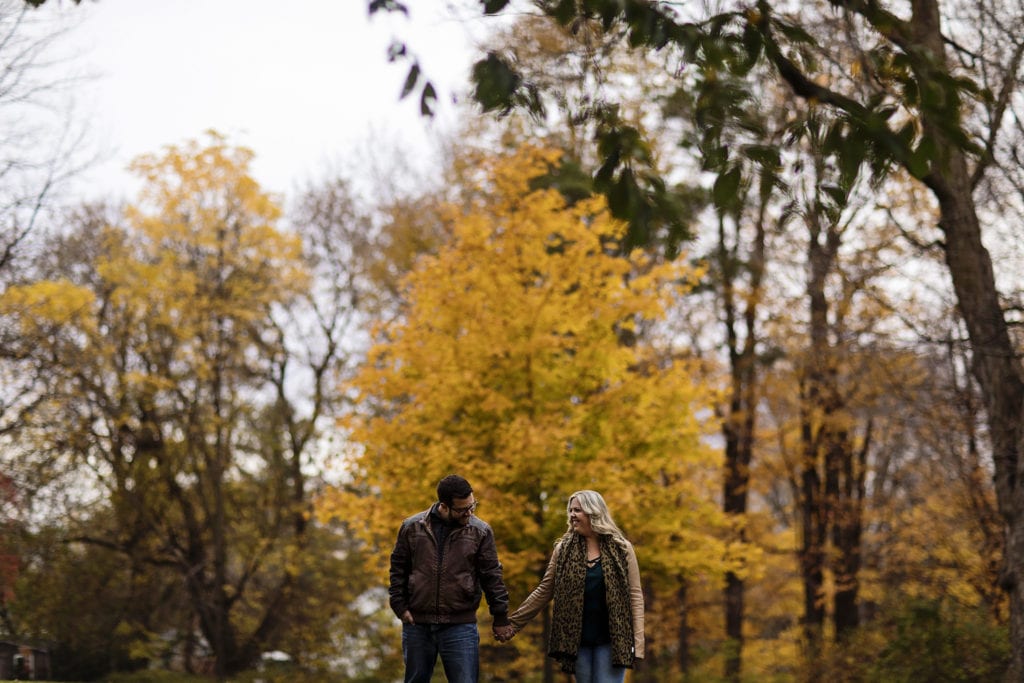 couple walking hand in hand against brilliant fall trees at Williamstown Engagement Session
