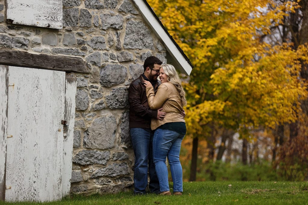 couple leaning against aged stone building with brilliant fall colors during Williamstown Engagement Session