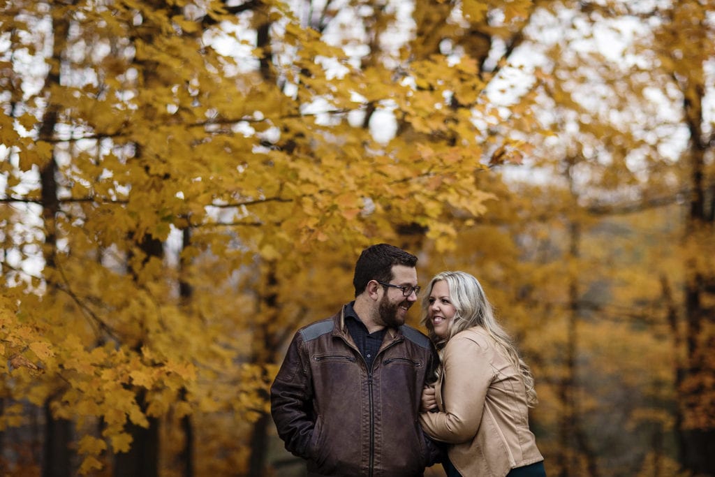 couple in leather jackets giggling in fall colored forest during Williamstown Engagement Session