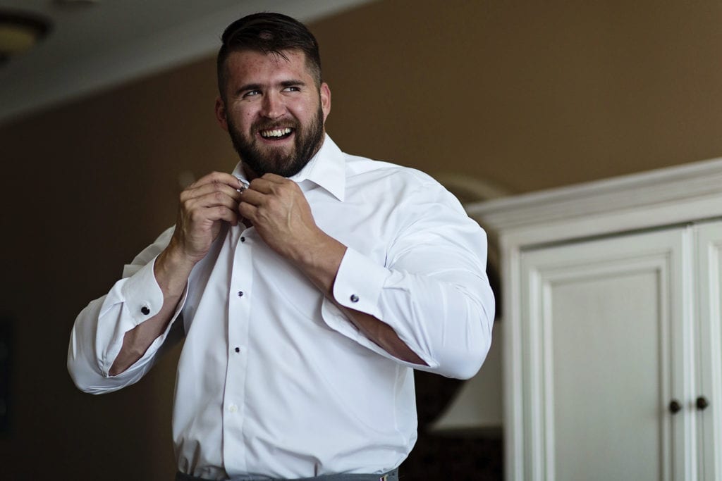 groom laughs and looks sideways as he fastens collar button