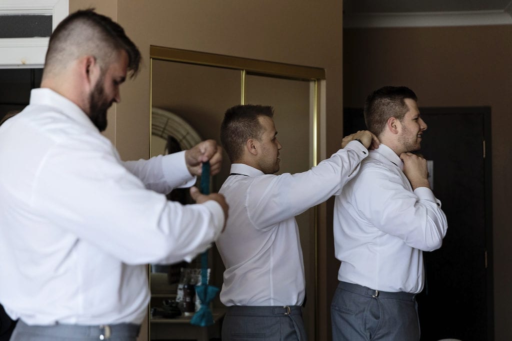 man helps friend with bow tie as groom adjusts length of his