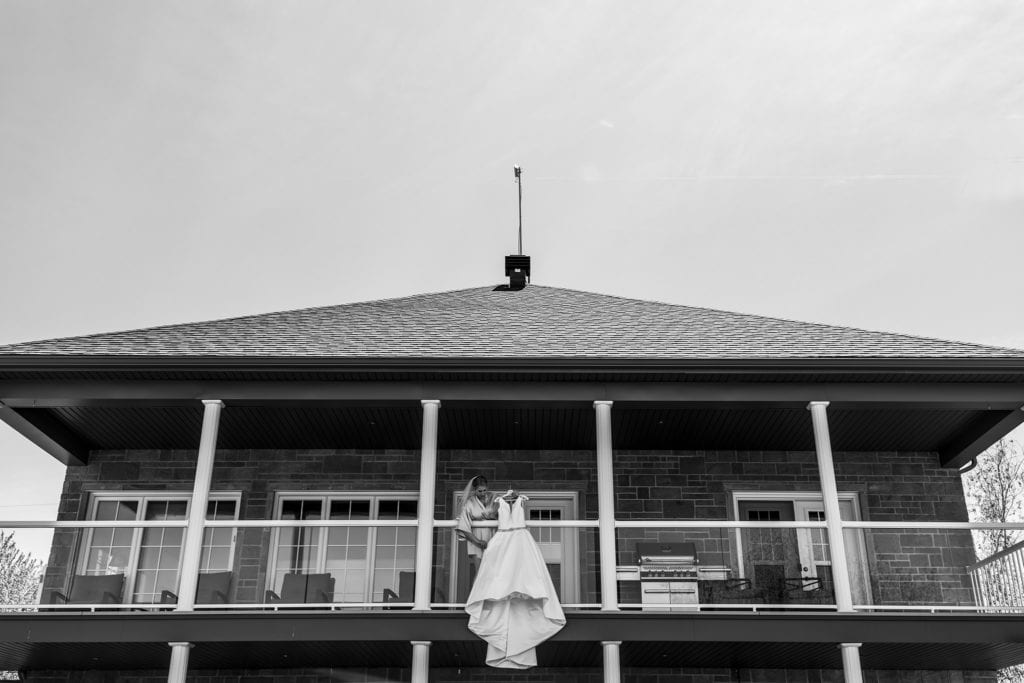 bride stands on balcony hanging dress over railing