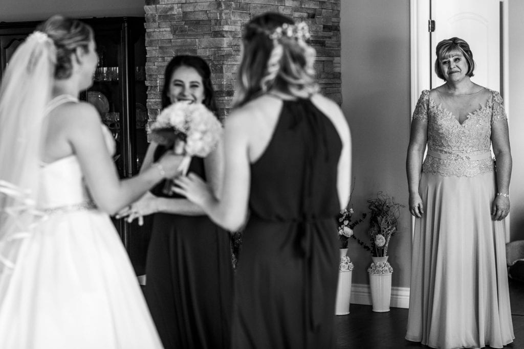 mother looks on as bride gets ready with bridesmaids