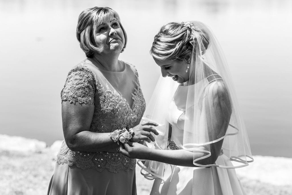 mother looks up at sky while trying not to cry as bride places corsage on her wrist