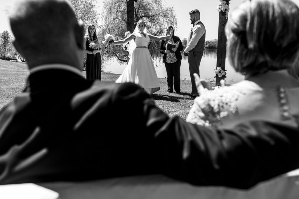 bride does funny dance step and looks surprised during Plantagenet wedding ceremony while father sits with arm around wife