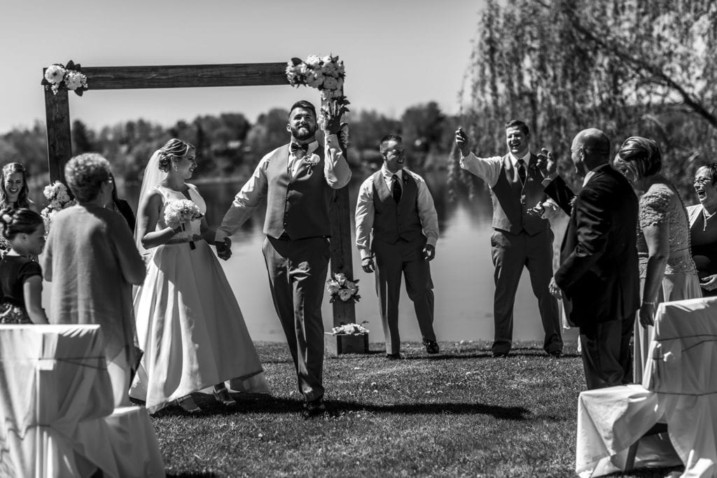 groomsman throws grass like confetti and groom pretends to catch it while walking down aisle after Plantagenet wedding reception