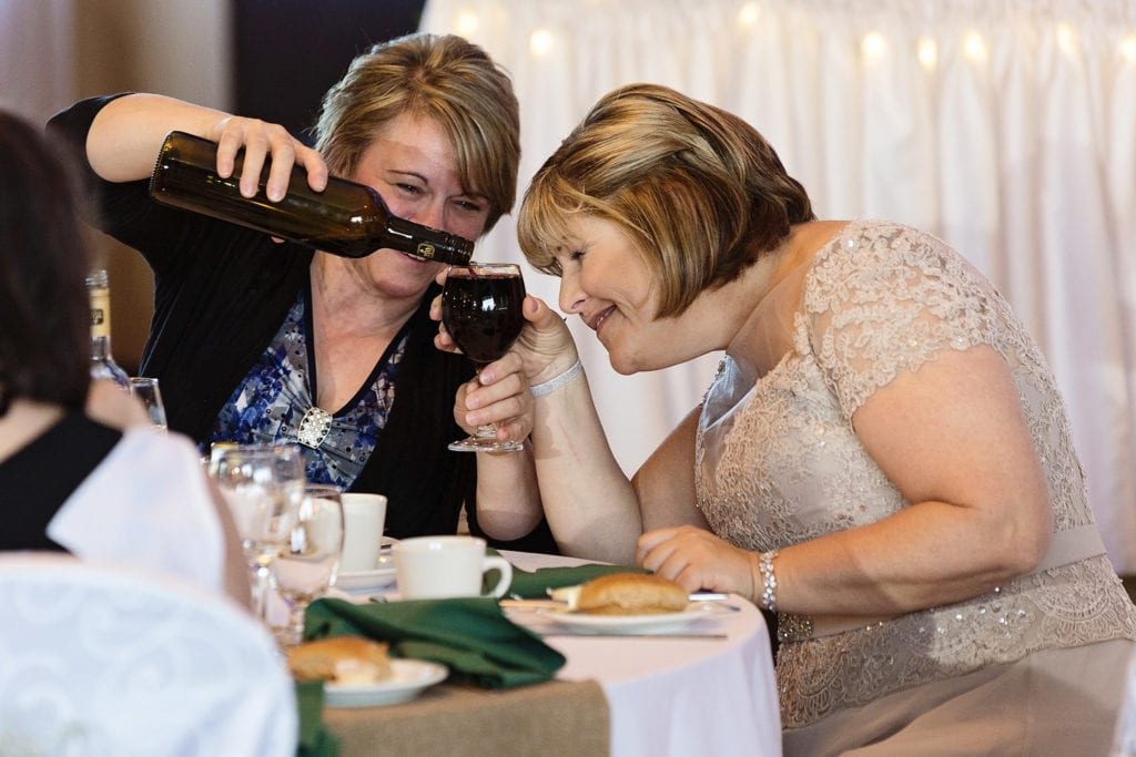 woman fills wine glass to brim while woman holding it squints to check if it's full
