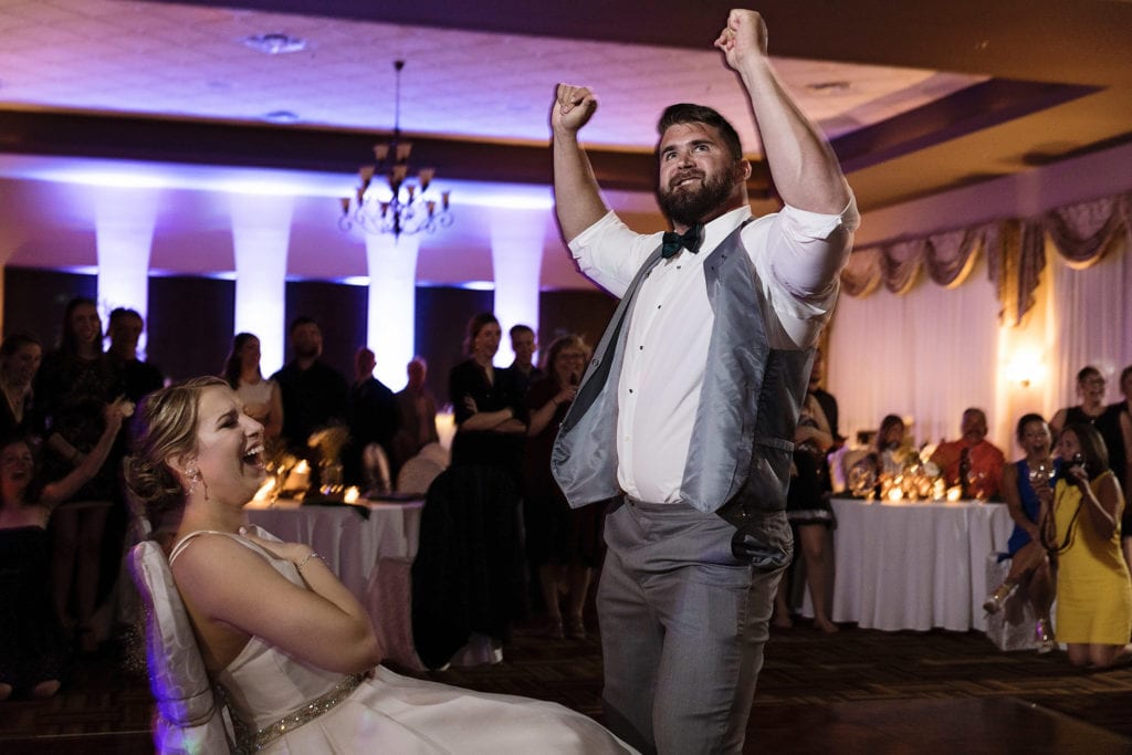 bride laughs while groom dances in front of her chair