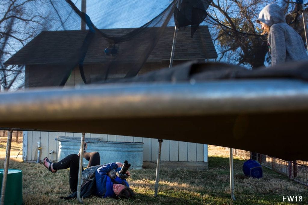 woman lying on back under trampoline with dog jumping on her