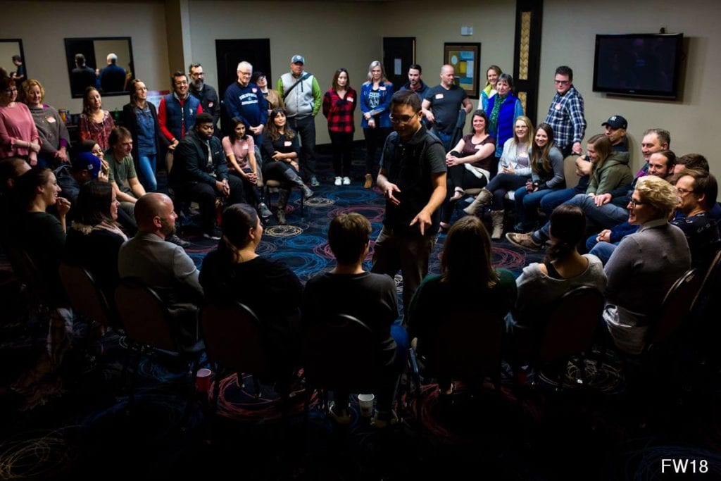 group of people sitting in circle with one man in centre pointing finger at someone