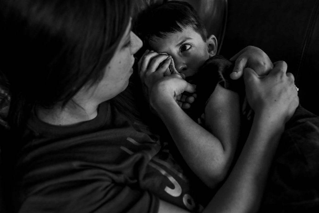 boy holds cloth to eye and looks at mother