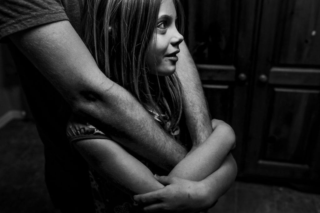 girl stands with dad's arms wrapped around her