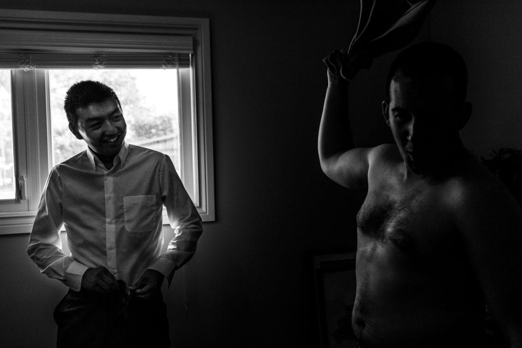 Groom gets ready while groomsman throws off shirt