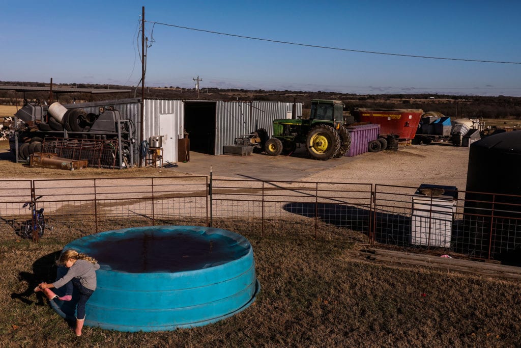 girl empties boot while standing next to upside down pool with farm in background