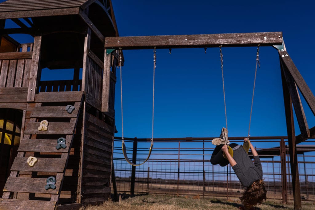 girl hangs upside down on swing