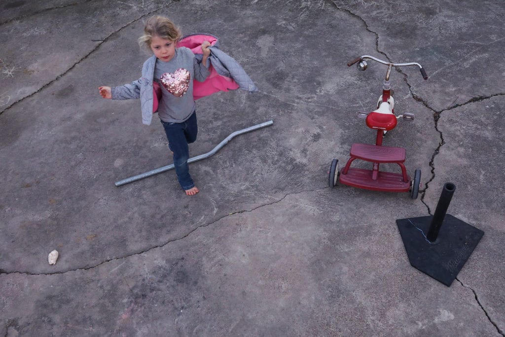 girl steps over length of pipe lying on cracked concrete