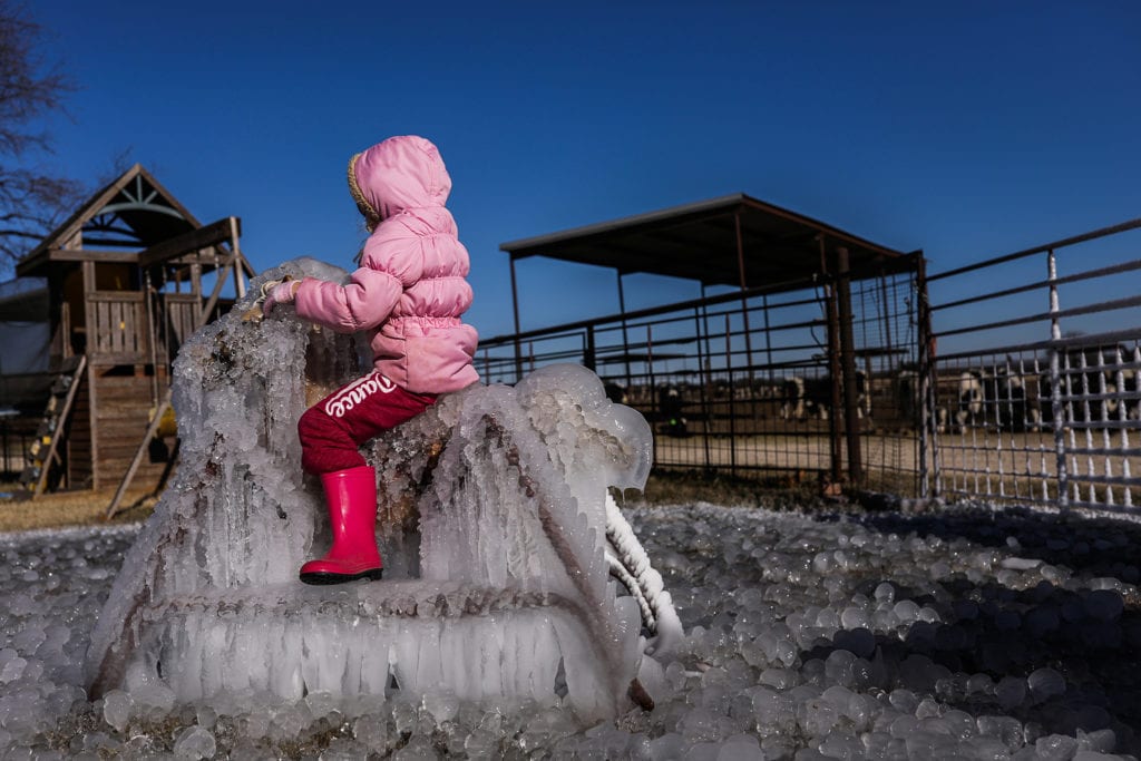 girl in pink coat sits on frozen hobby horse